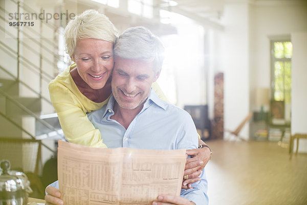 Ältere Frau umarmt Mann beim Zeitungslesen