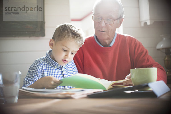 Junge liest mit Großvater bei Tisch