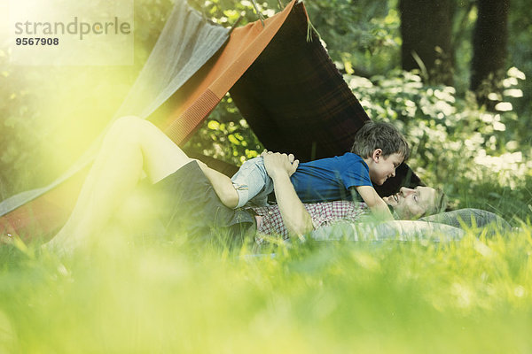 Vater und Sohn liegen im Gras in der Nähe des Campingzeltes