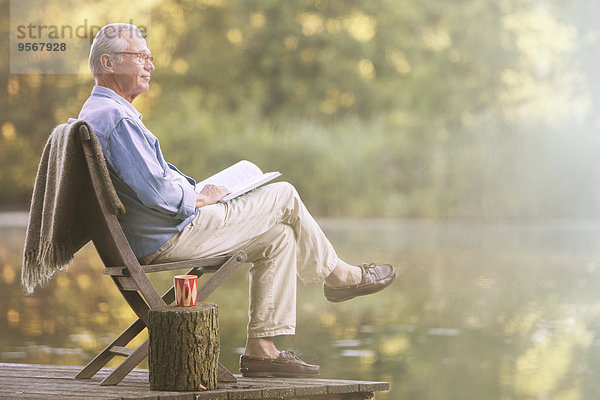 Älterer Mann liest Buch am Dock am See