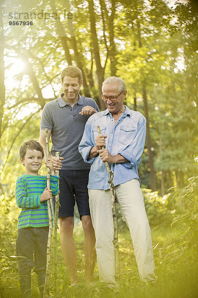 Junge  Vater und Großvater halten Stöcke im Wald.