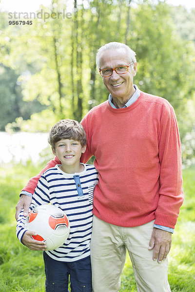 Großvater und Enkel lächeln im Freien mit Fußball