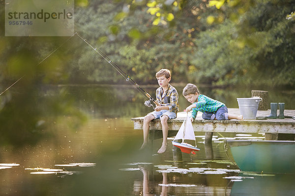 Jungen fischen und spielen mit Spielzeug-Segelboot am See