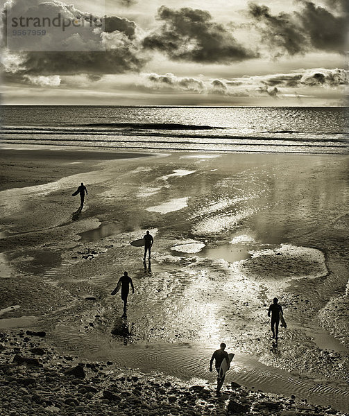 Silhouetten von Surfern  die mit Surfbrettern am Perranuthnoe Beach spazieren gehen.