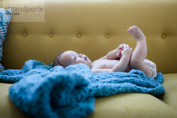 Kleines Baby auf blauem Tuch liegend mit erhobenen Beinen  einen Fuß haltend