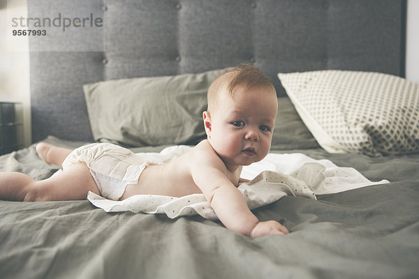 Porträt des kleinen Babys auf dem Bett liegend mit erhobenem Kopf