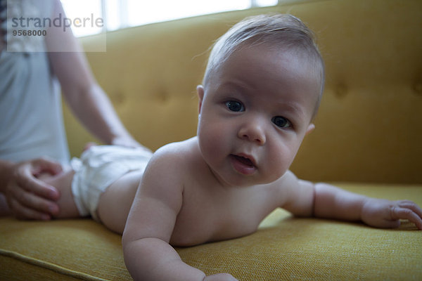 Porträt des kleinen Babys auf dem gelben Sofa liegend  mit Blick auf die Kamera