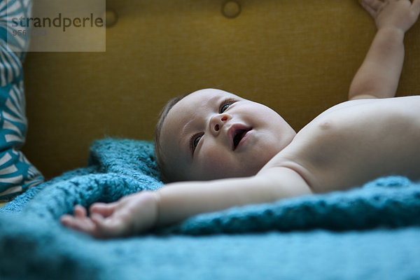 Porträt eines lächelnden Babys auf blauem Stoff liegend mit ausgestreckten Armen