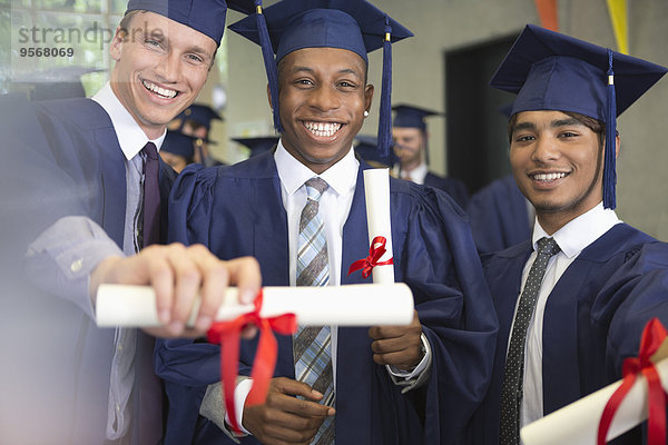 Porträt von lächelnden Universitätsstudenten  die nach der Abschlussfeier ein Diplom besitzen