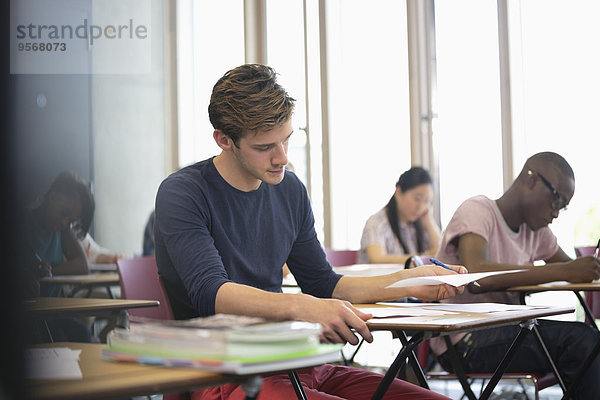 Universitätsstudent beim Examen  Studenten beim Schreiben im Hintergrund