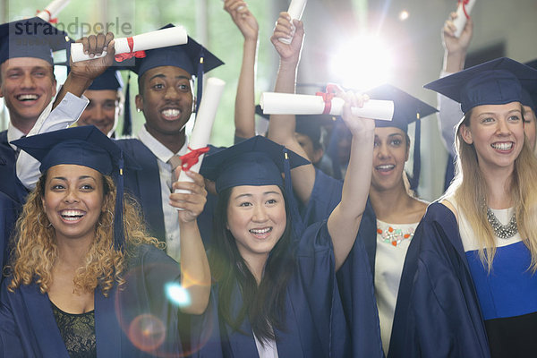 Lächelnde Universitätsstudenten stehen mit ihren Diplomen nach der Abschlussfeier im Flur