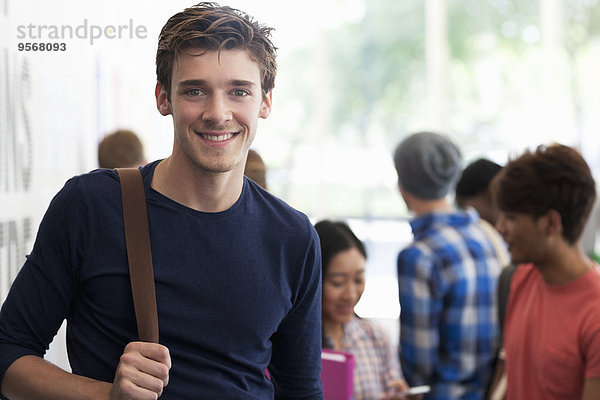 Porträt eines lächelnden Studenten  der in der Pause im Flur steht  Menschen im Hintergrund sprechend