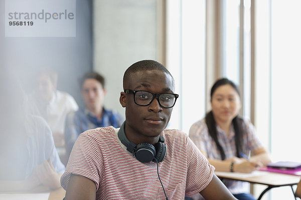 Männlicher Student mit Brille und Kopfhörer um den Hals  der während der Vorlesung auf die Kamera schaut.