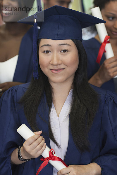 Studentin lächelt vor der Kamera und hält Diplom