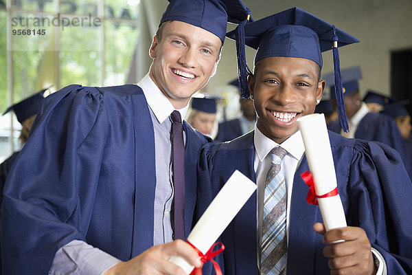 Zwei lachende männliche Studenten in Diplom-Kleidung