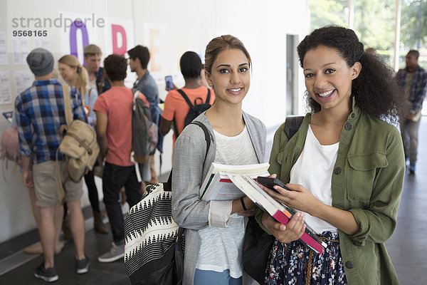 Porträt von zwei lächelnden Studentinnen mit Büchern  andere Studenten im Hintergrund