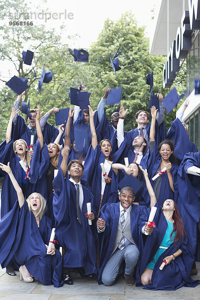 Gruppenporträt von Studenten in Promotionskleidern  die Mörtelbretter in die Luft werfen.