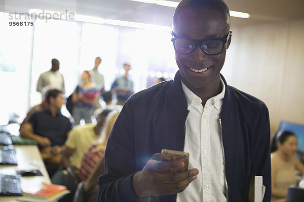 Lächelnder Schüler mit Brille  der auf das Smartphone schaut  mit anderen Schülern im Hintergrund