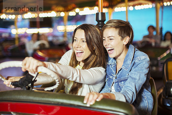 Zwei fröhliche Frauen auf Stoßstange Autofahrt im Vergnügungspark