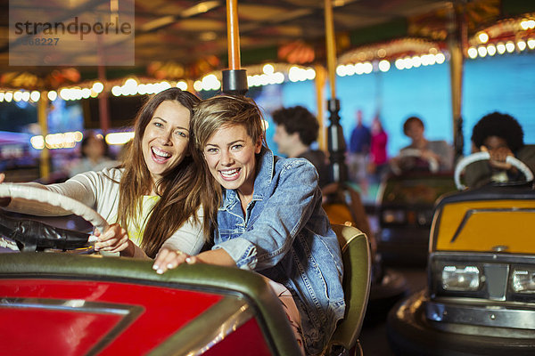 Zwei fröhliche Frauen auf Stoßstange Autofahrt im Vergnügungspark