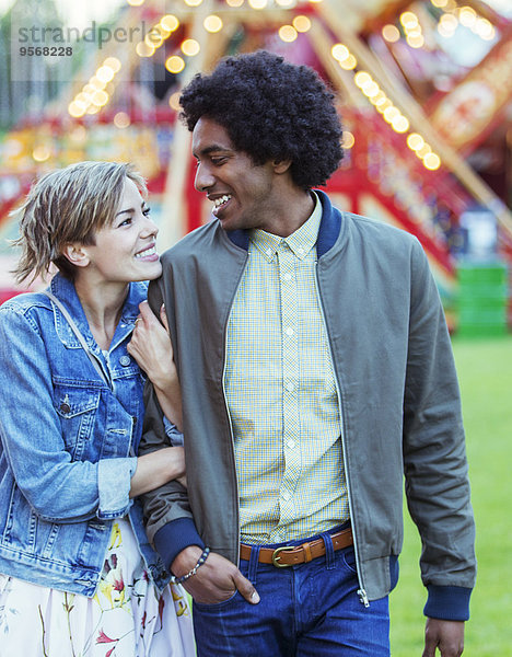 Junges multirassisches Paar lächelt sich in einem Vergnügungspark an.