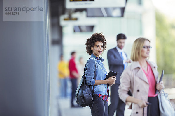 Frau hält digitales Tablett und wartet auf Zug im Bahnhof