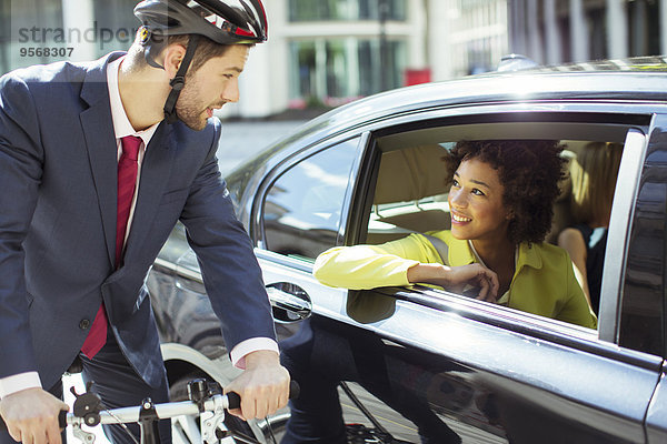 Geschäftsmann auf dem Fahrrad im Gespräch mit Frau im Auto