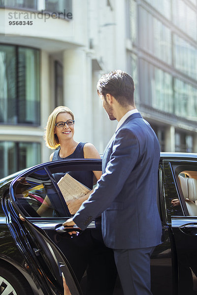 Chauffeur öffnet Autotür für Geschäftsfrau