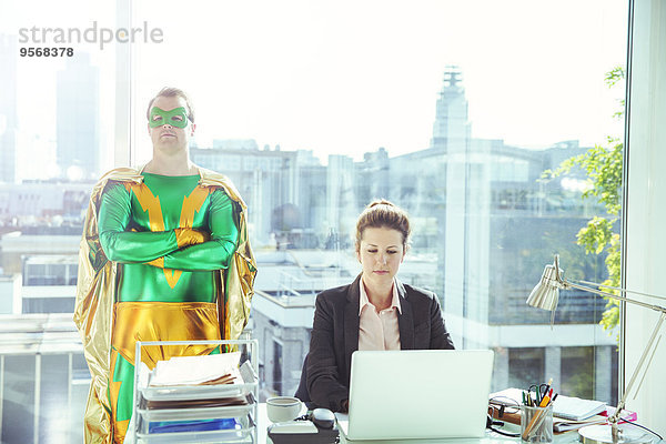 Superheldin in der Nähe einer Geschäftsfrau  die im Büro arbeitet.