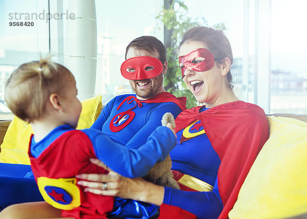 Superhelden-Eltern spielen mit Tochter auf dem Wohnzimmersofa