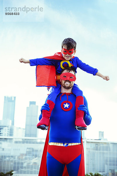 Superhelden-Vater mit Sohn auf den Schultern auf dem Dach der Stadt