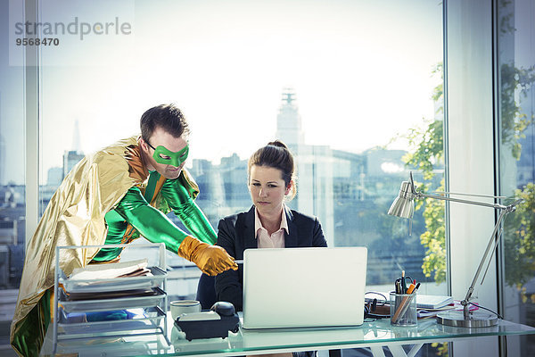 Superheldin hilft Geschäftsfrau bei der Arbeit am Schreibtisch