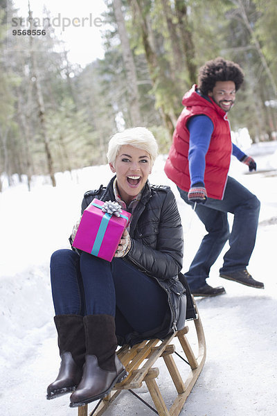 Mann zieht Frau mit Geschenk auf Schlitten im Schnee