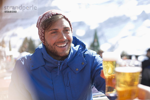 Lächelnder Mann in warmer Kleidung trinkt Bier im Freien