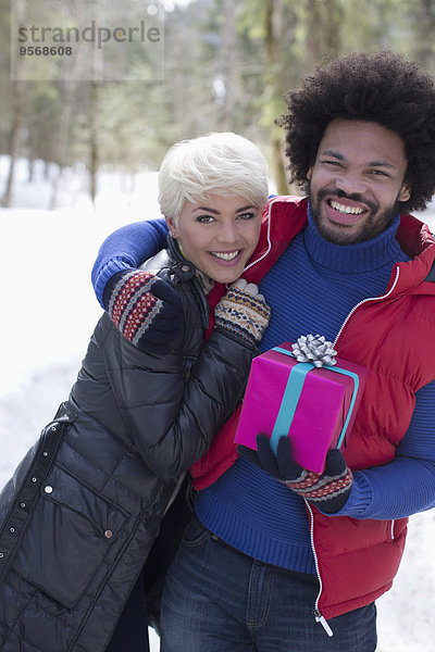 Porträt eines Paares mit Weihnachtsgeschenk im Schnee