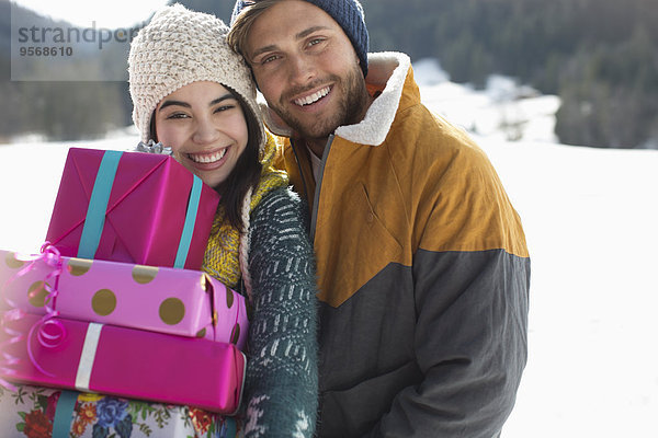 Porträt eines lächelnden Paares mit Weihnachtsgeschenken im Schnee