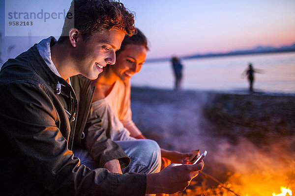 Handy nahe Zusammenhalt benutzen Europäer Strand Feuer