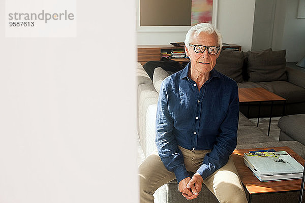 Porträt eines älteren Mannes mit Brille in seinem Wohnzimmer