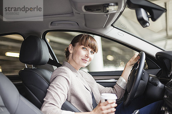 Deutschland  Hessen  Frankfurt  Porträt einer lächelnden Geschäftsfrau mit Kaffee zum Mitnehmen im Auto