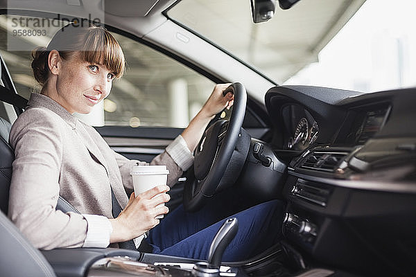 Deutschland  Hessen  Frankfurt  Porträt einer lächelnden Geschäftsfrau beim Autofahren mit Kaffee in einer Hand