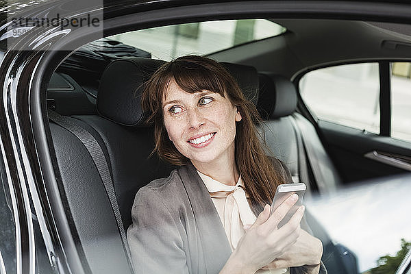 Deutschland  Porträt einer lächelnden Geschäftsfrau im Auto mit Smartphone