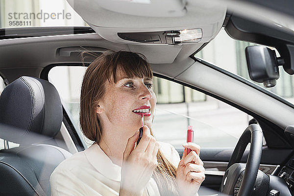 Porträt einer Geschäftsfrau  die im Auto sitzt und Lippenstift aufträgt