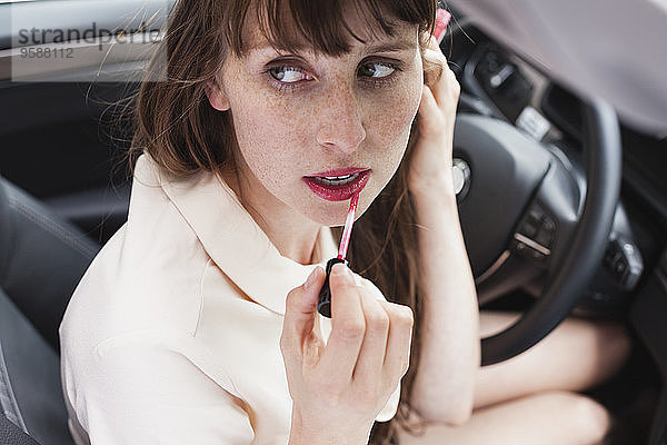 Porträt einer Geschäftsfrau  die im Auto sitzt und Lippenstift aufträgt