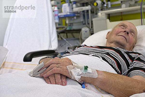 Älterer Mann mit Kanülen und Pflaster auf der Intensivstation nach Herzinfarkt