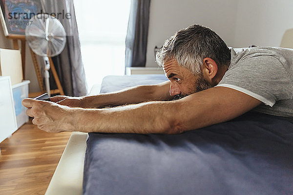 Mann  der auf seinem Bett liegt und einen Selfie mit seinem Smartphone nimmt.