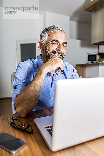 Porträt eines lächelnden Geschäftsmannes bei der Arbeit mit dem Laptop im Home Office