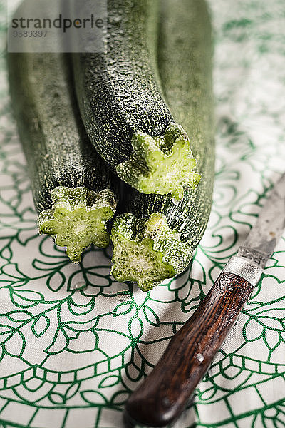 Drei Zucchini und ein altes Messer auf Tuch