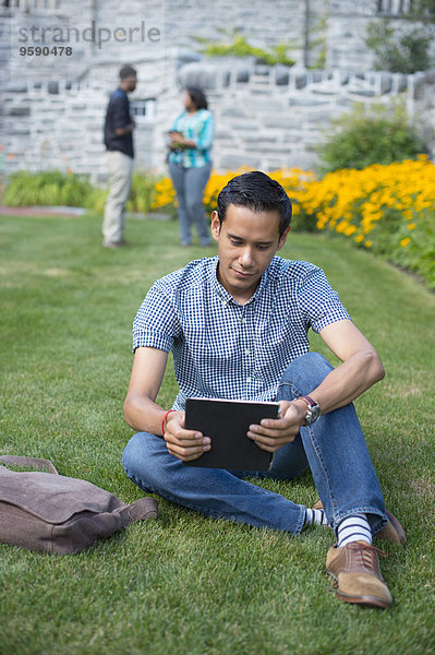 Männlicher Schüler auf Rasen sitzend mit digitalem Tablett