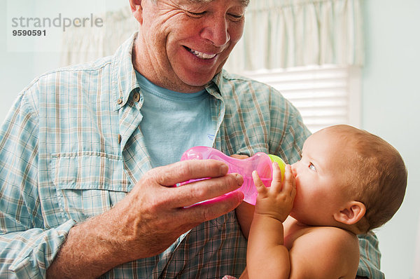 Großvater Flasche Fütterung Baby Enkelin auf Schoß im Wohnzimmer