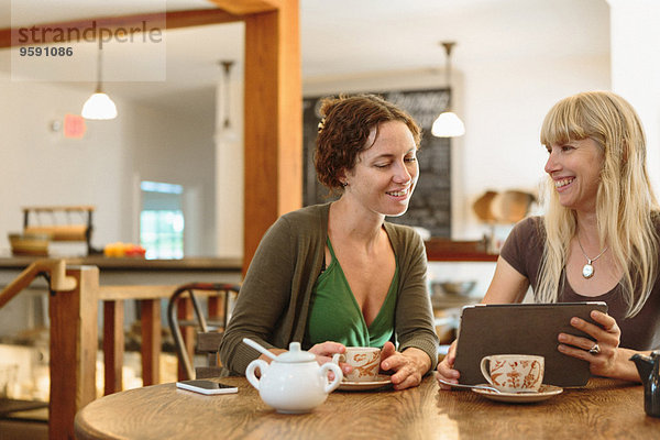 Zwei mittlere erwachsene Freundinnen beim Betrachten des digitalen Tabletts im Country Store Cafe